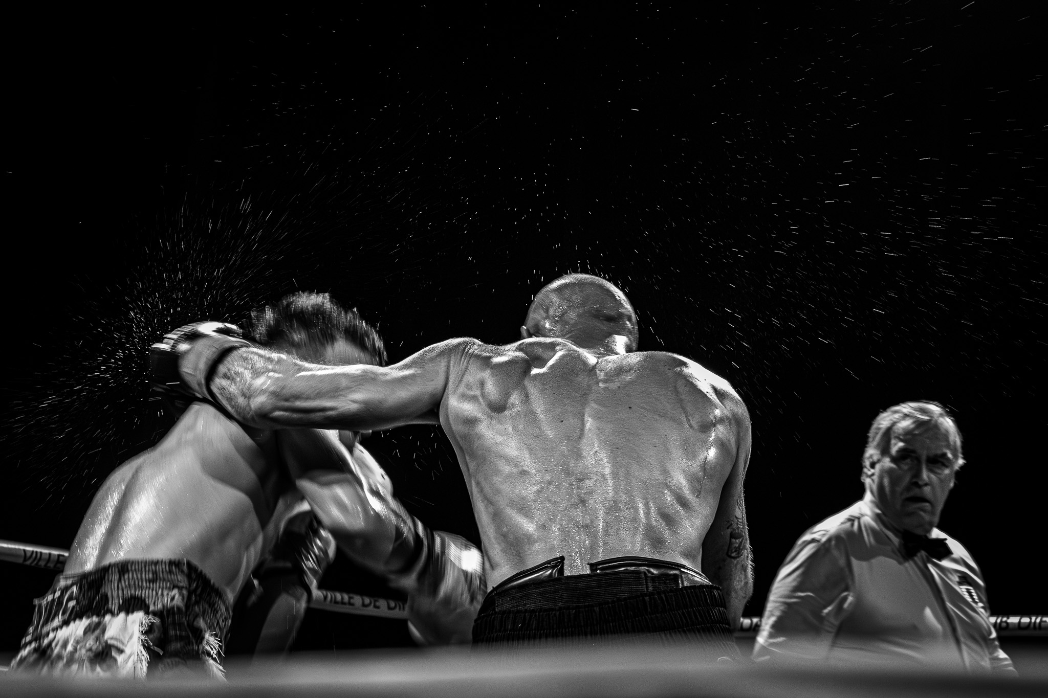 Boxer delivering a powerful punch to opponent's head with referee watching closely
