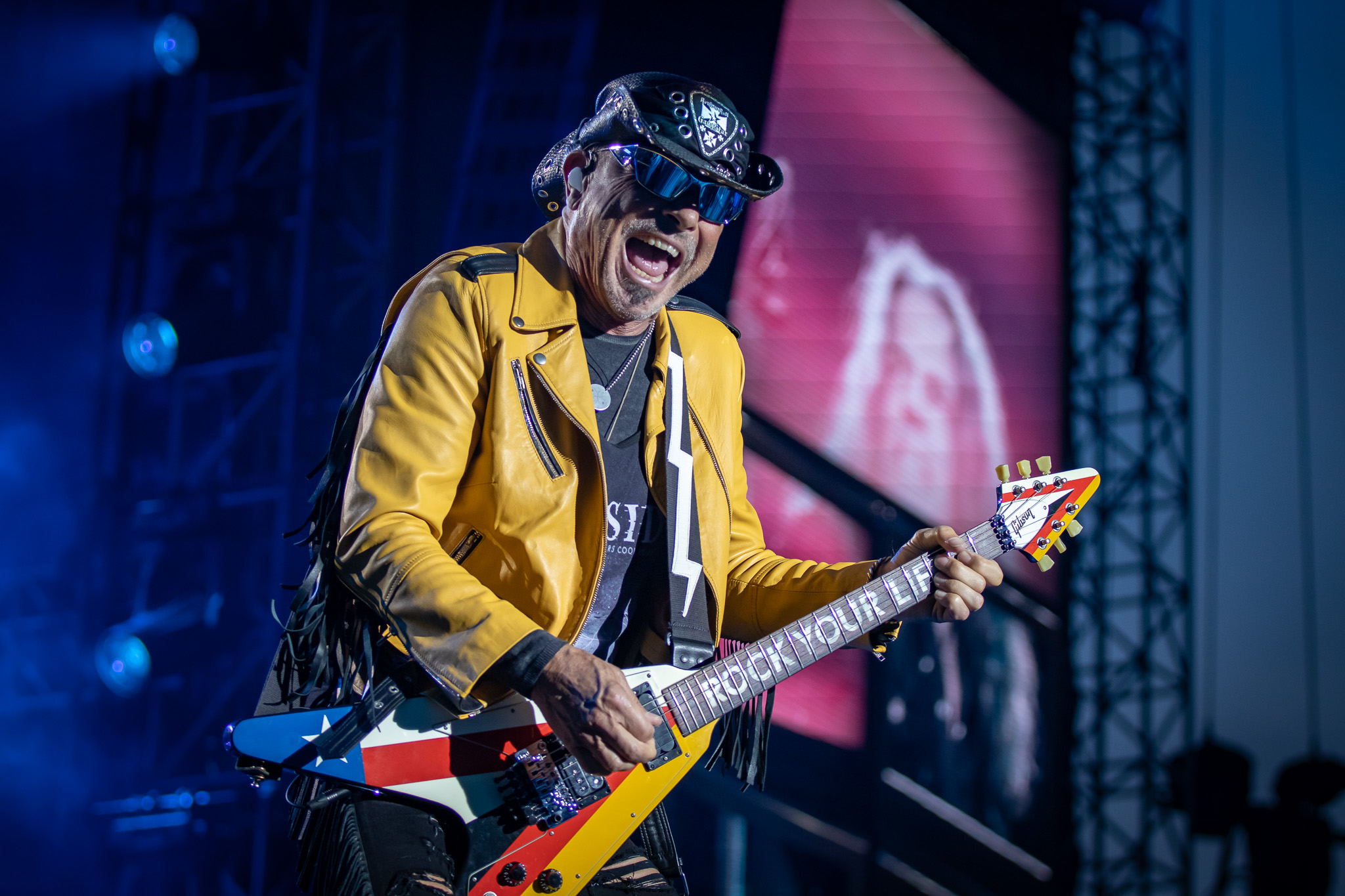 A rock guitarist in a yellow leather jacket performing on stage, playing a colorful electric guitar with a lively expression.