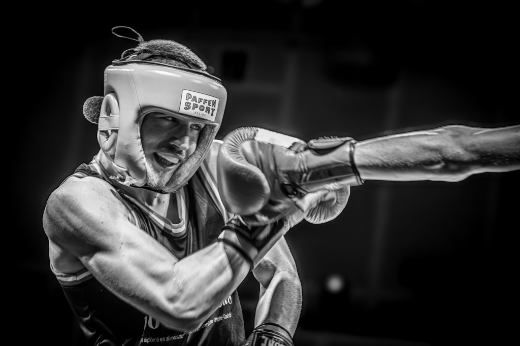 A black and white image of a boxer wearing protective headgear, receiving a punch.
