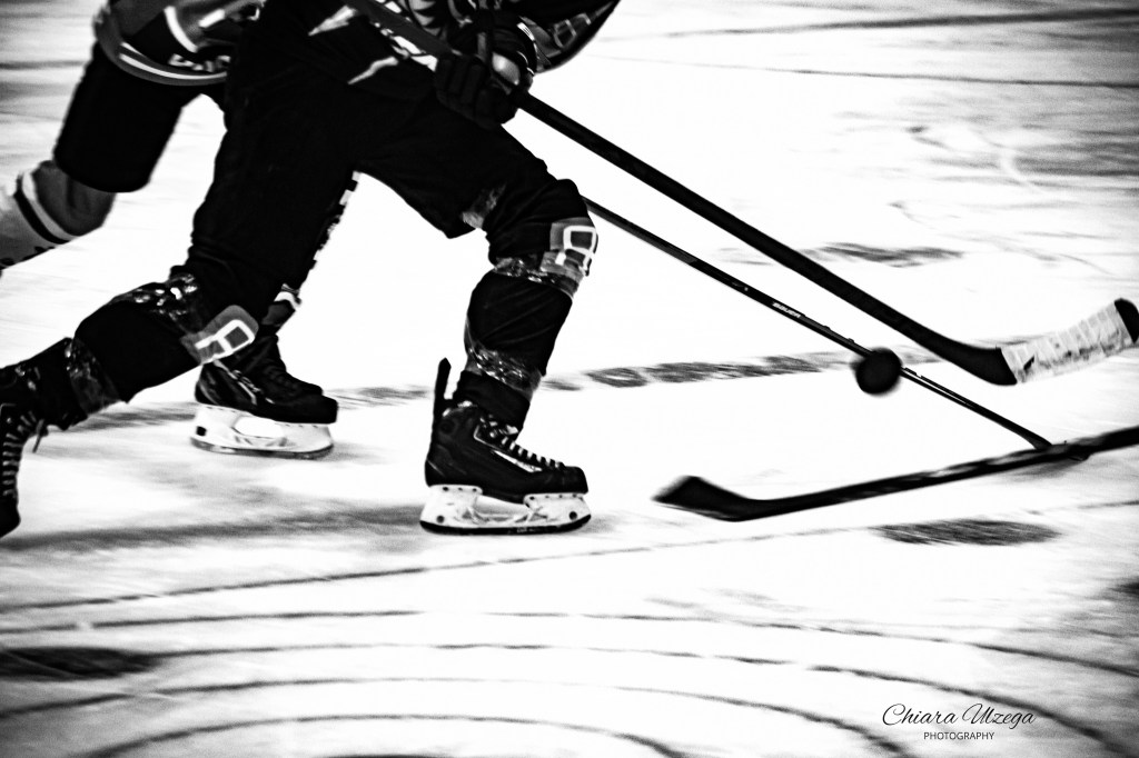 A dynamic black and white image of ice hockey players in motion, focusing on a player skating and handling the puck.