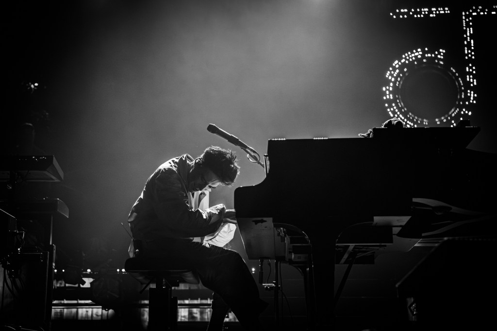 Grammy winner Jacob Collier playing piano on stage in a black and white dramatic photo