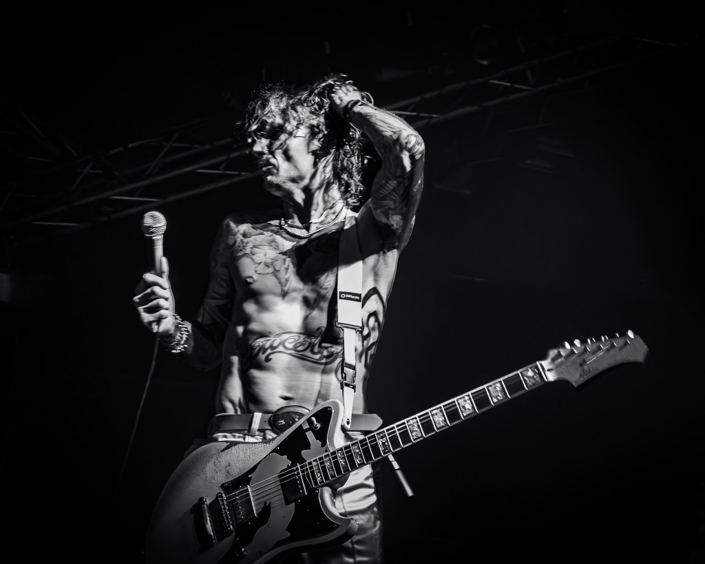 Justin Hawkins bare-chest with tattoos and guitar on stage
