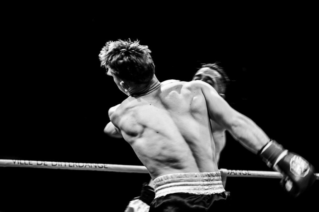 Black and white image of two boxers in action, focusing on one fighter delivering a powerful punch, seen form the back.