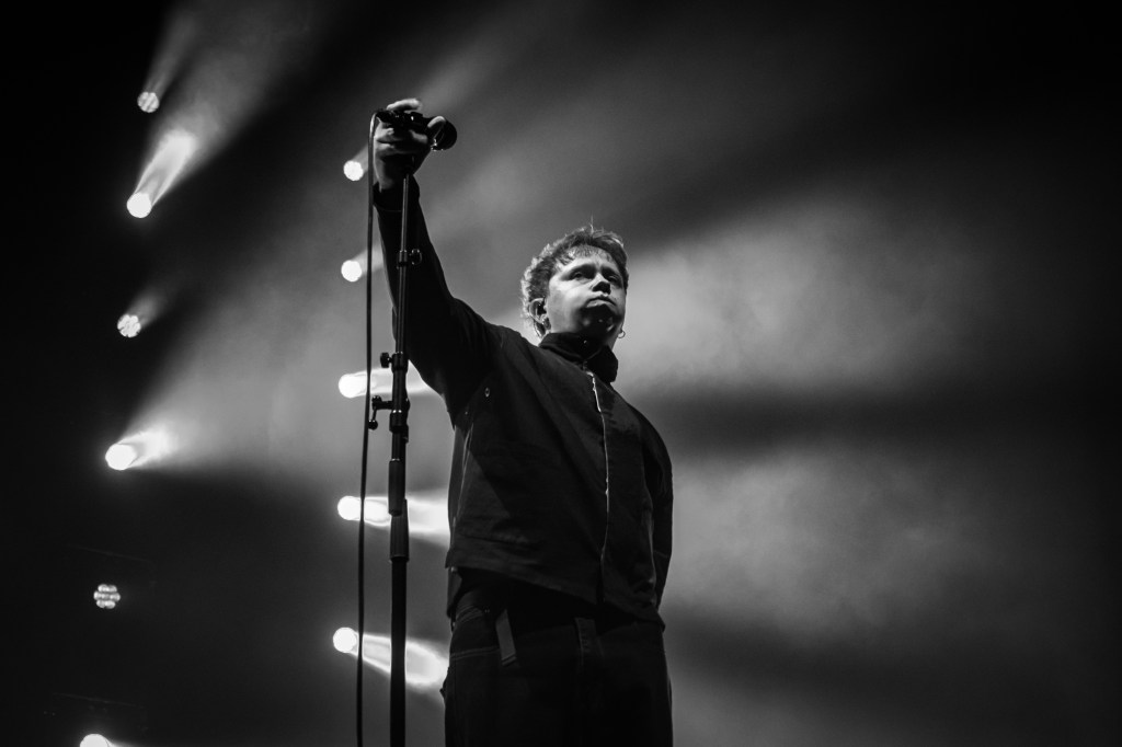 A lead singer standing confidently on stage with a microphone in hand, illuminated by dramatic lighting, creating a powerful black and white image.