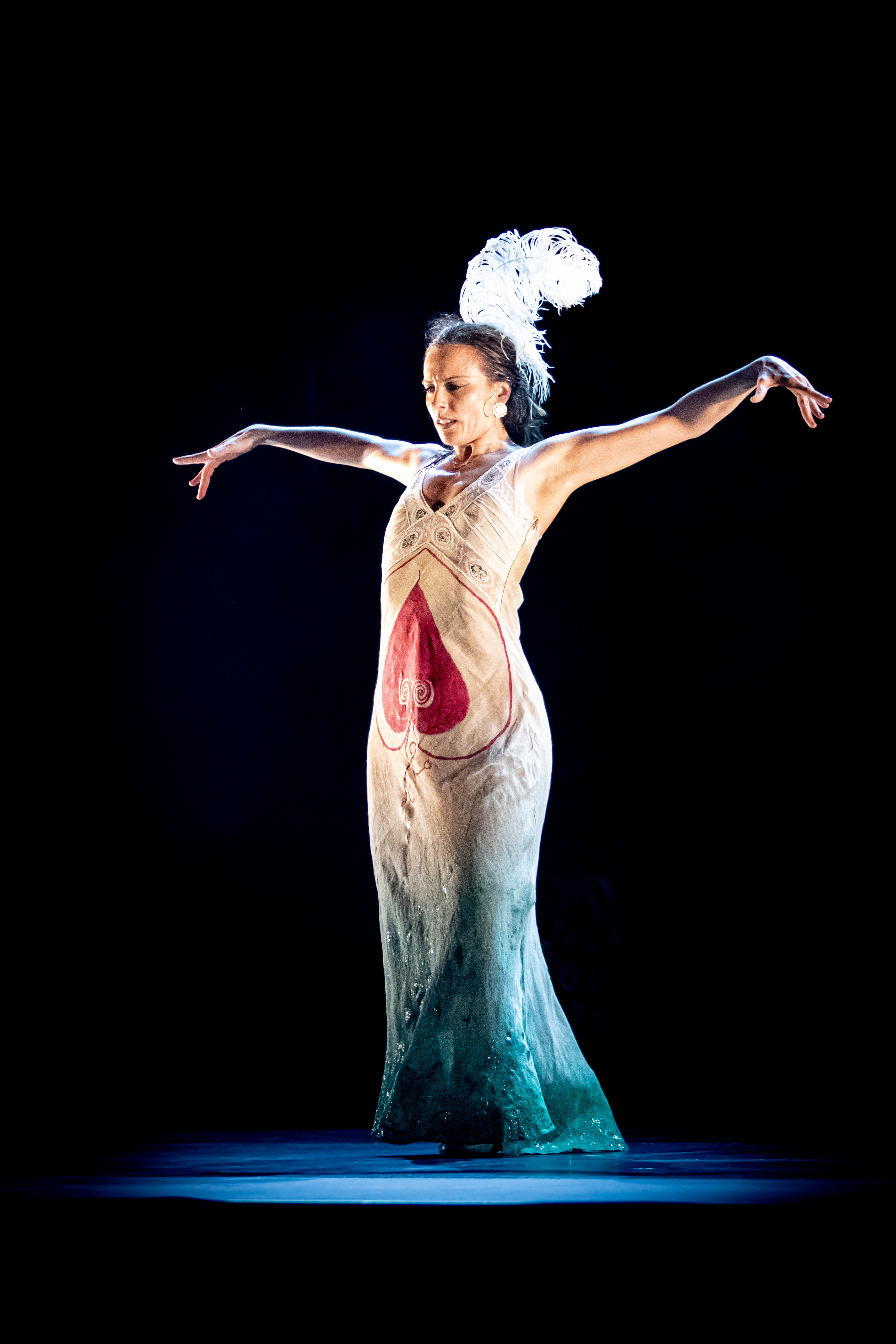 A dancer in an ornate dress with a feathered headpiece poses gracefully against a dark background.