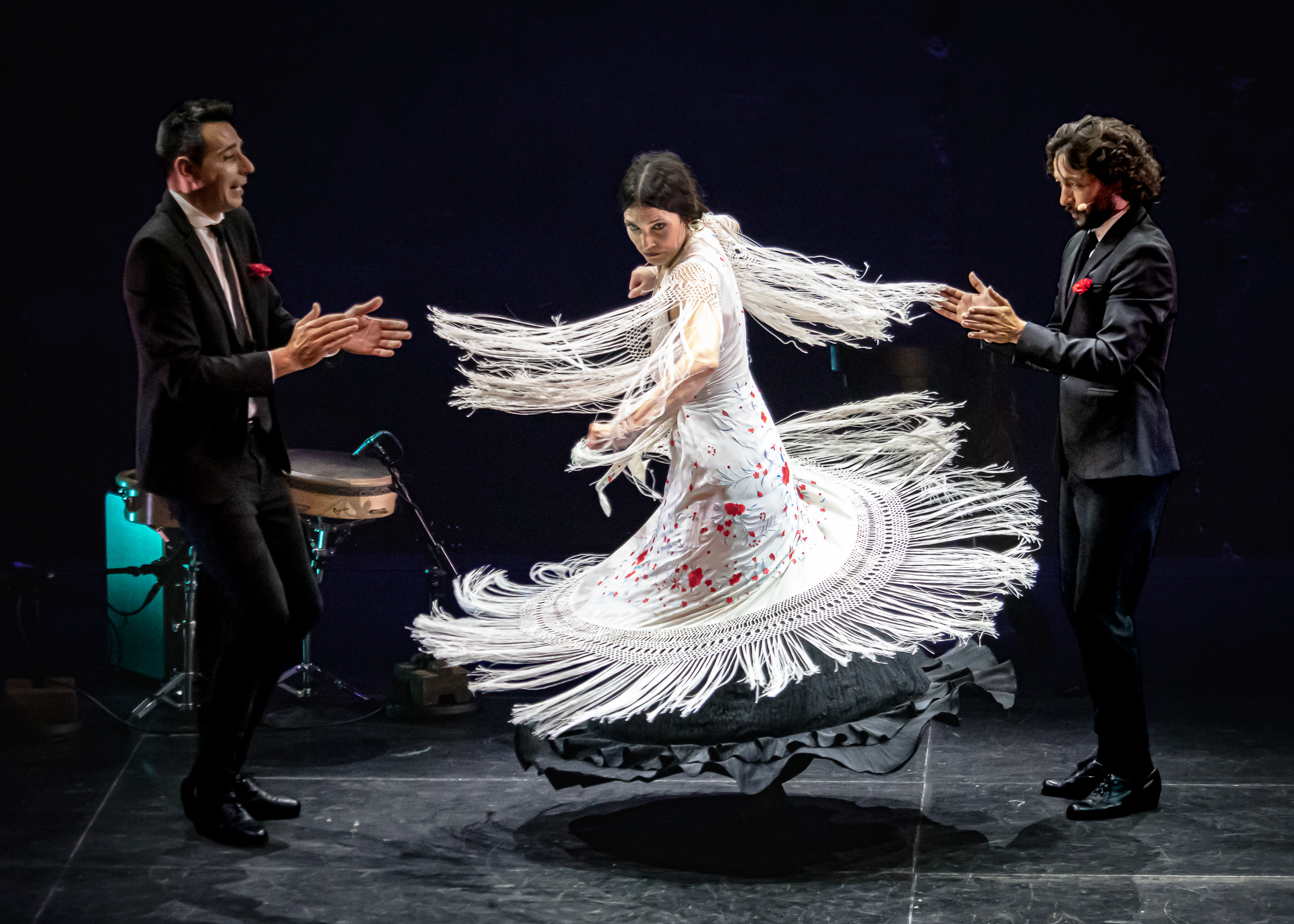A dancer in a fringed flamenco dress spins between two musicians in black suits