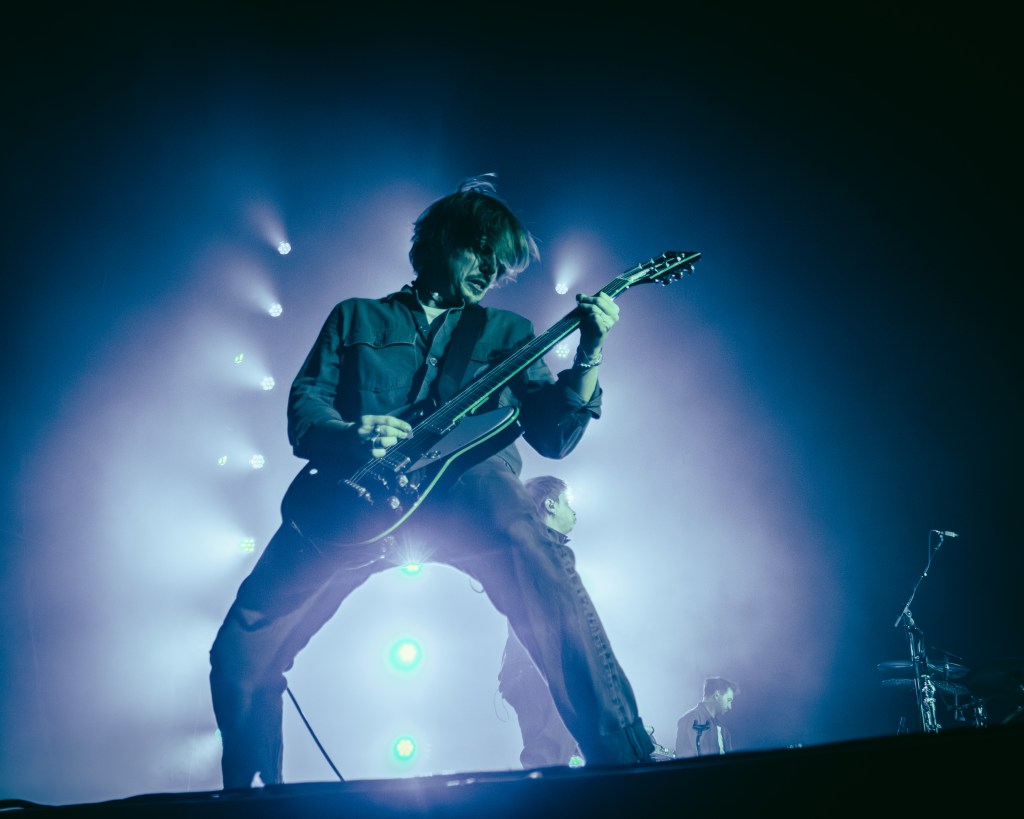 A guitarist energetically playing on stage with vibrant lighting, captured in a moment of intense performance, hair flowing and focused on the music.