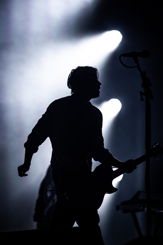 A silhouette of a guitarist on stage, striking a pose with his instrument, set against a backdrop of dramatic light beams.