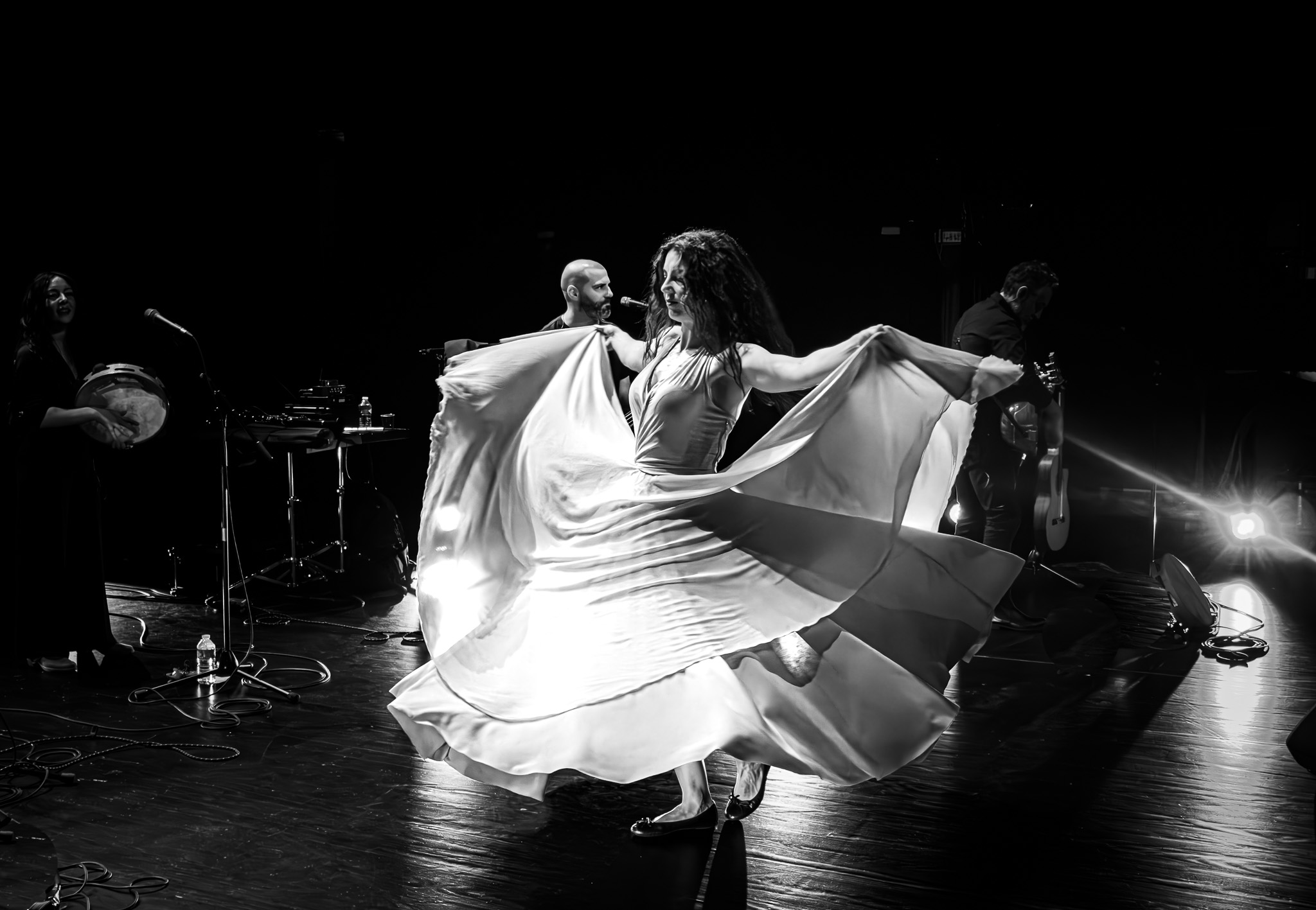 A dancer twirls in a flowing dress, creating a swirl of fabric, while musicians play instruments in the background.