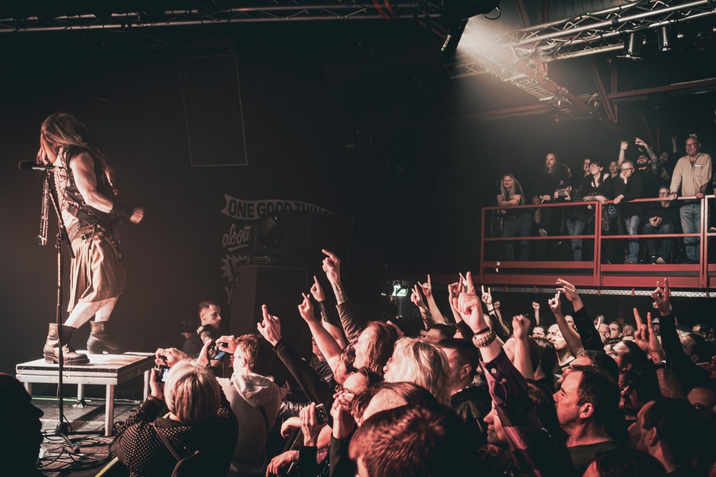 Zakk Wylde performing on stage while the energetic crowd cheers and raises their hands in excitement