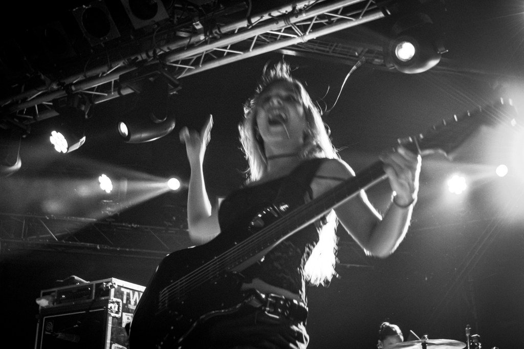A guitarist passionately performing on stage, captured in motion with an energetic expression. Bright stage lights illuminate the scene, highlighting the intensity of the performance