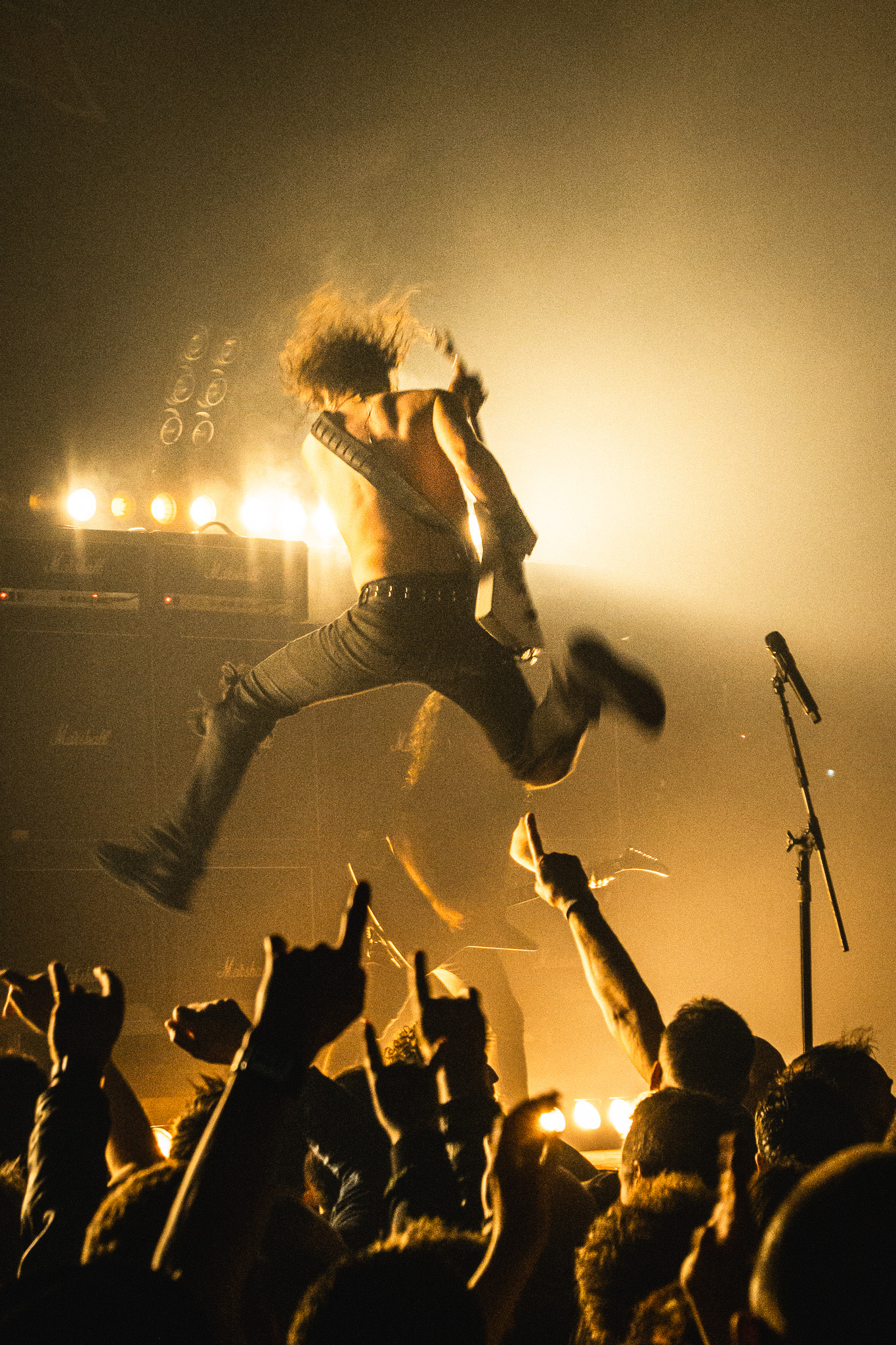A rock guitarist mid-air jumping during a live concert stage performance.