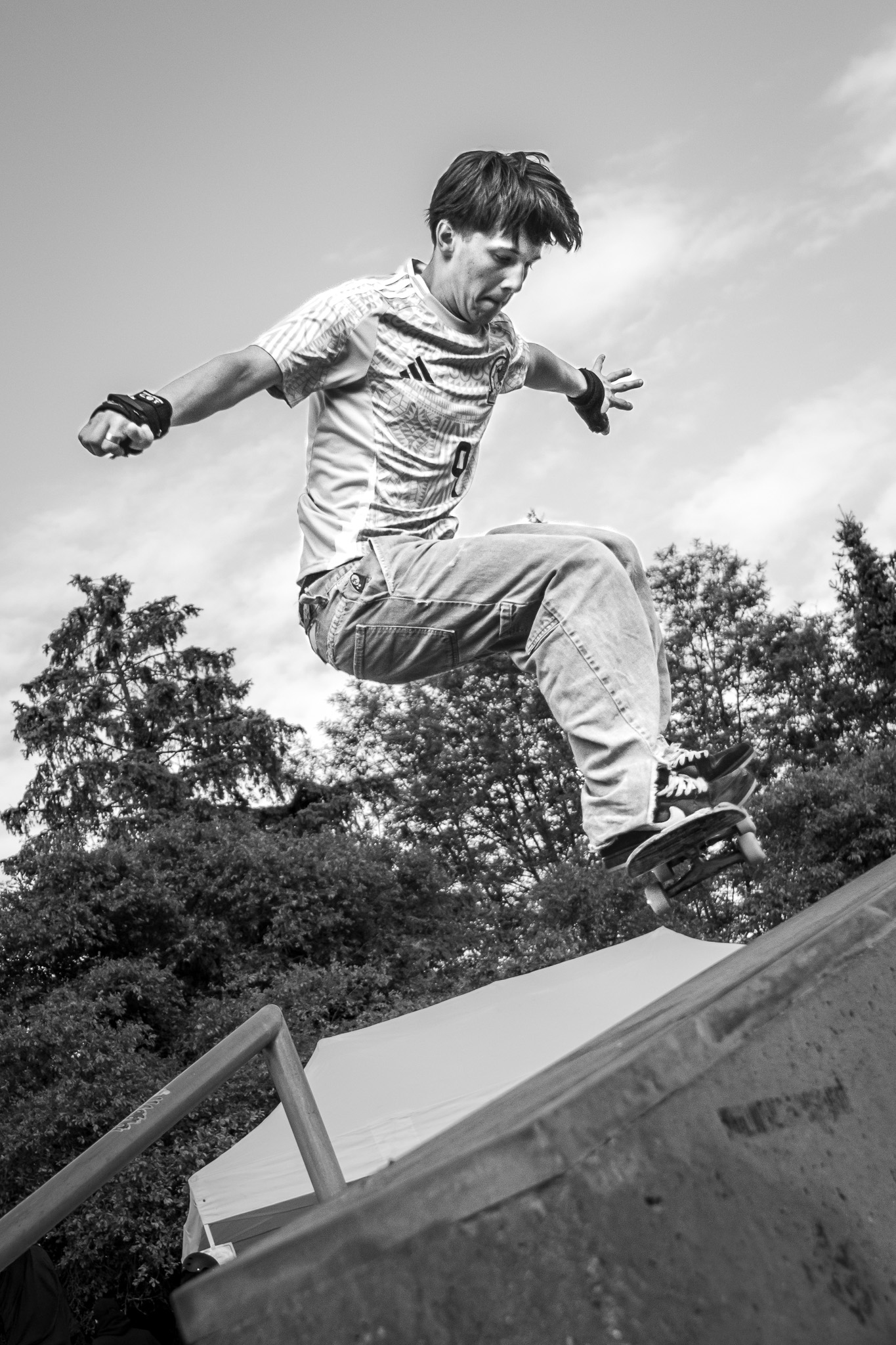 Teenager performing a skateboard jump at a skate park under a cloudy sky